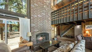 Una sala de estar acogedora con chimenea, una escalera y un ventanal grande con vistas a un bosque.