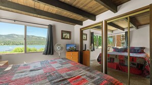 Un dormitorio con una cama grande, un aparador, un ventilador, un televisor y vistas a un lago y montañas.