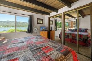 Ein Schlafzimmer mit einem großen Bett, einem Schminktisch, einem Ventilator, einem Fernseher und Blick auf einen See und Berge.