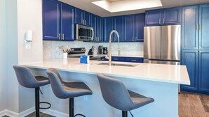 Une cuisine moderne avec des meubles bleus, des appareils en acier inoxydable et un îlot central doté de tabourets de bar.