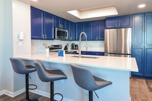 A modern kitchen with blue cabinets, stainless steel appliances, and a central island with bar stools. - 11th Floor- Easy Walk to Beach - 2BR Palms of Destin 11001 (Destin)