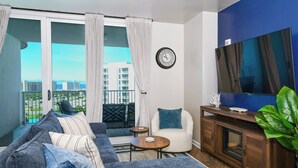 Un salon comprenant un canapé, un fauteuil, une table basse, un téléviseur et un balcon avec des rideaux.
