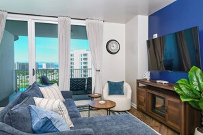 A living room with a sofa, armchair, coffee table, TV, and balcony with curtains. - 11th Floor- Easy Walk to Beach - 2BR Palms of Destin 11001 (Destin)