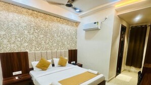 A hotel room with a large bed, a headboard with a floral pattern, a wooden nightstand, an air conditioning unit, and a door with curtains. - DD Green Residency (New Delhi)