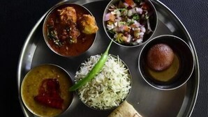 A meal served on a metal plate with various dishes including rice, a curry, a salad, a bread roll, and a dessert. - DD Green Residency (New Delhi)