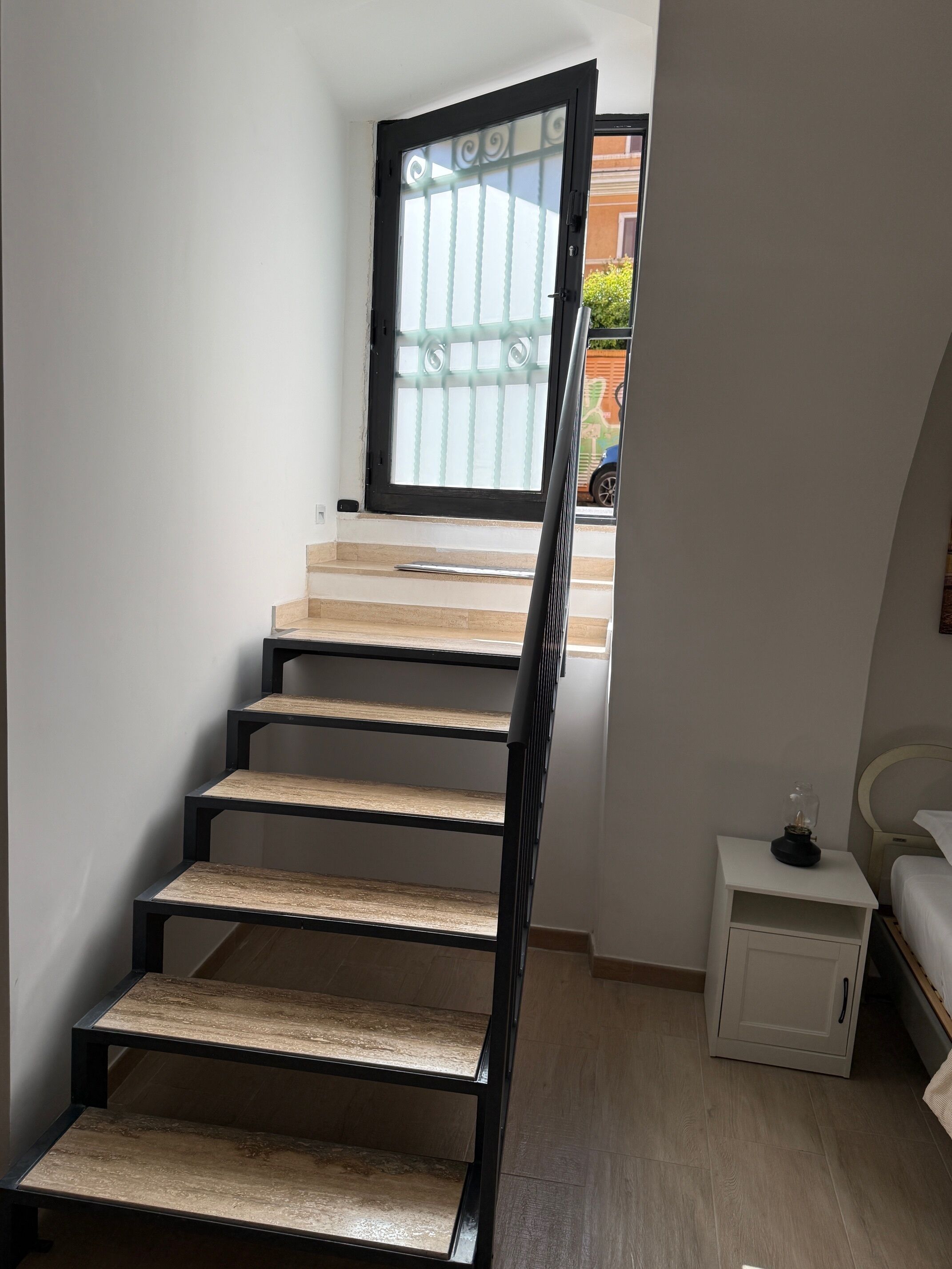 A staircase with wooden steps and black railings, leading to a room with a bed and a small bedside table.
