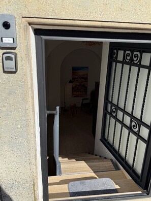 Une porte avec un portail en métal, une petite marche menant à l’intérieur et un interphone fixé au mur.
