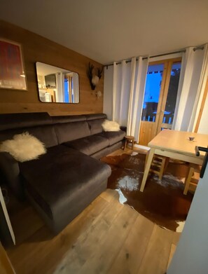 A living room with a dark brown sofa, a white fluffy pillow, a wooden dining table, and a wooden floor. - Sunny apartment just a 3-minute walk from the slopes (Chalon-sur-Saône)