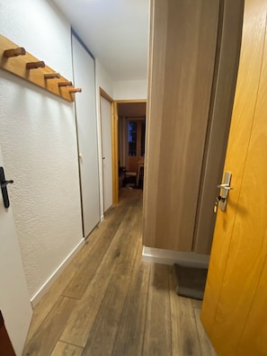 Een gang met houten vloer, een kapstok en een deur naar een andere kamer.