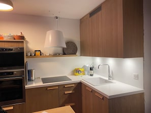 Una cocina moderna con armarios de madera, horno empotrado, lavabo e iluminación colgante.