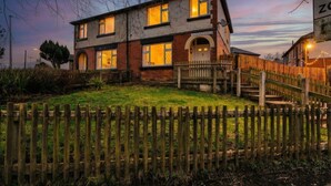 A two-story house with a front porch, a wooden fence, and a sign indicating a property for sale. - Newly Refurbished 3BR Home Parking Sleeps 5 (Bolton)