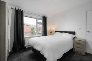 Une chambre à coucher comprenant un lit, une table de chevet, une lampe, une fenêtre avec des rideaux et une vue sur l’extérieur.