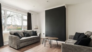 A modern living room with two grey sofas, a small wooden table, and a large black accent wall. - Newly Refurbished 3BR Home Parking Sleeps 5 (Bolton)