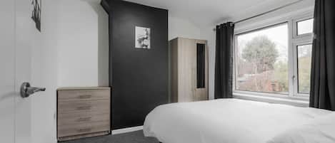 Un dormitorio con cama, cómoda, armario, ventana y un cuadro en la pared.