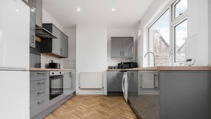 A modern kitchen with grey cabinets, a herringbone floor, and a window providing natural light. - Newly Refurbished 3BR Home Parking Sleeps 5 (Bolton)