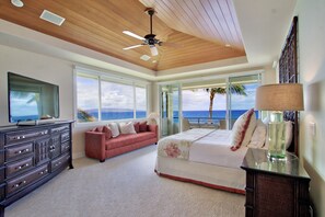 A bedroom with a bed, a dresser, a red sofa, and large windows with a view of the ocean.