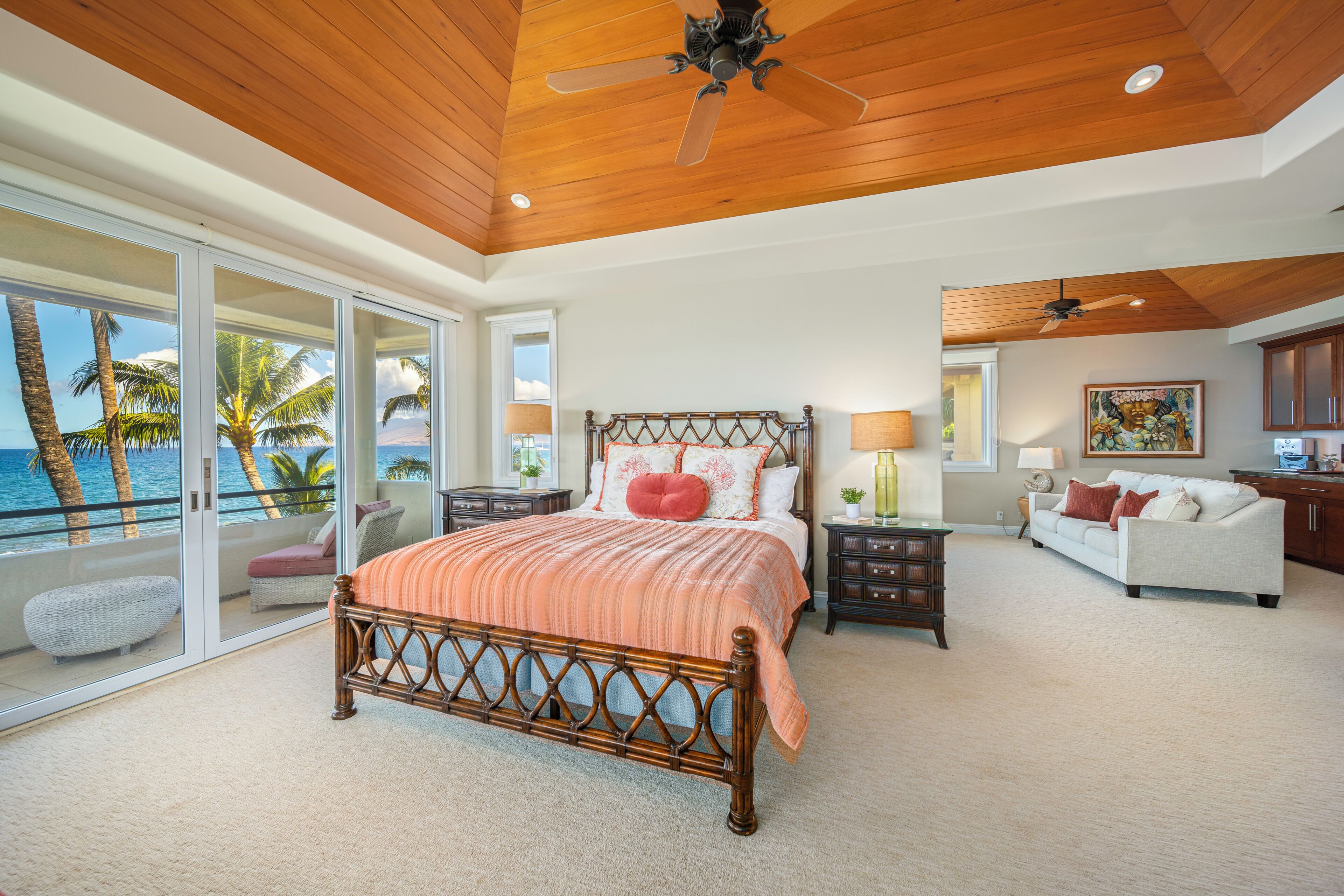 A spacious bedroom with a large bed, a balcony with a view of the ocean, and a ceiling fan.