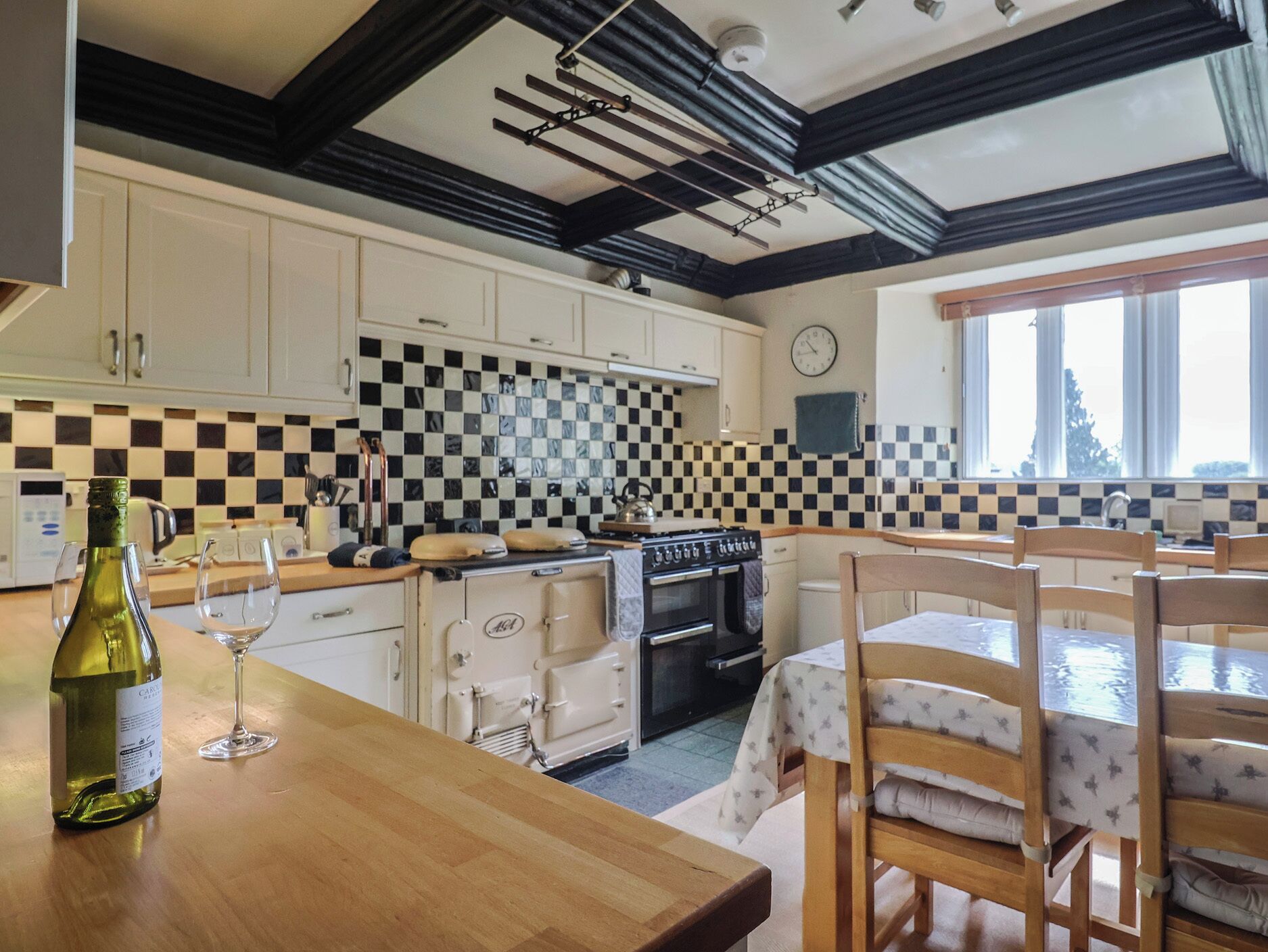 A kitchen with white cabinets, a checkered backsplash, a wooden table, and a window.