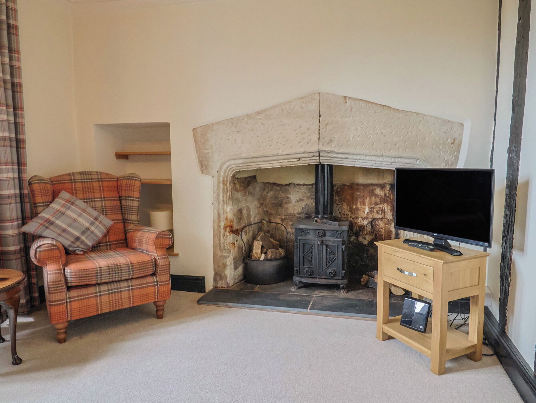 A living room with a fireplace, a plaid sofa, a television on a wooden stand, and a plaid curtain.