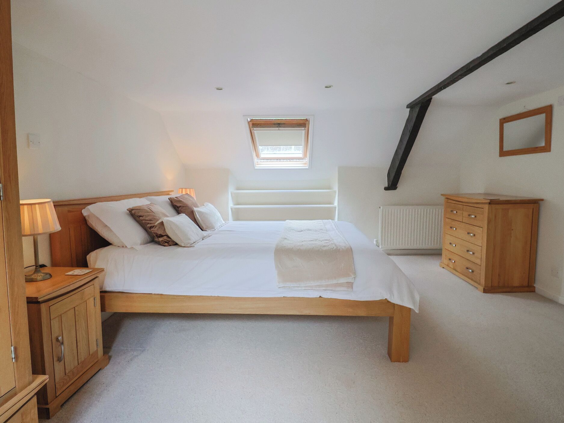 A bedroom with a bed, a nightstand, a dresser, a radiator, and a skylight.