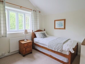 A bedroom with a single bed, a nightstand, a lamp, a window with curtains, a radiator, and a framed picture on the wall. - Ellishayes Farm (Honiton)