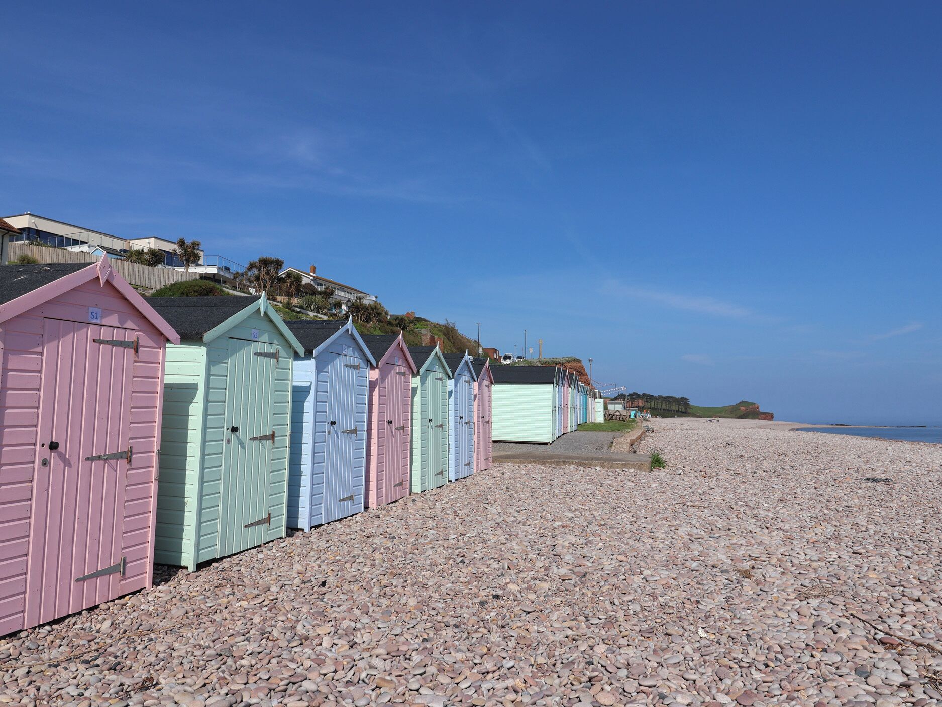 A row of beach huts with a pebble beach and a clear sky.