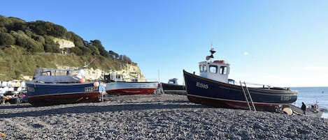 Boats docked on a pebbled beach with a cliff in the background.