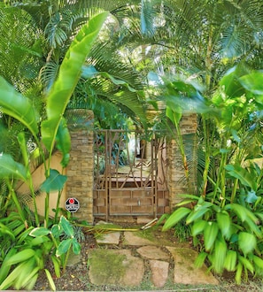 A gated entrance with a stone wall and metal gate, surrounded by lush tropical foliage. - FIVE BEDROOM BEACHFRONT HOME (Kihei)