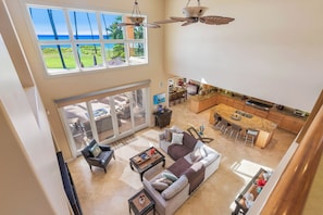 A spacious living area with a large window overlooking a lush landscape, a kitchen with modern appliances, and a dining area. - FIVE BEDROOM BEACHFRONT HOME (Kihei)