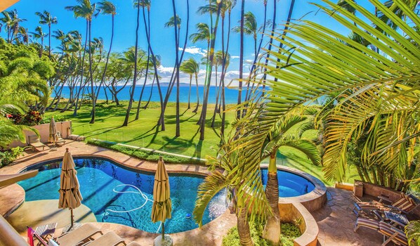 A pool area with lounge chairs and umbrellas, surrounded by palm trees and a view of the ocean. - FIVE BEDROOM BEACHFRONT HOME (Kihei)