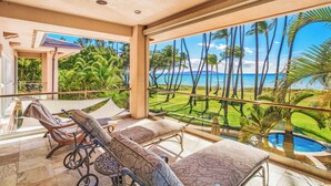 Ein Balkon mit Blick auf das Meer, ein Pool und eine Rasenfläche mit Palmen.