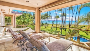 A balcony with a view of the ocean, a pool, and a lawn with palm trees. - FIVE BEDROOM BEACHFRONT HOME (Kihei)