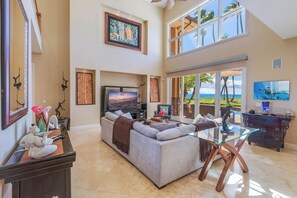 A spacious living area with a large sectional sofa, a glass coffee table, and a flat-screen TV. - FIVE BEDROOM BEACHFRONT HOME (Kihei)