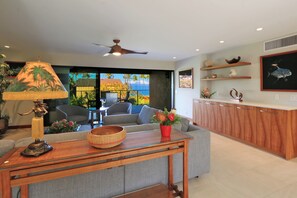 Ein modernes Wohnzimmer mit einer Couch, einem Esstisch, einem Deckenventilator und Blick ins Freie.
