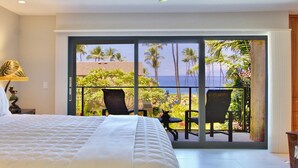 Een slaapkamer met een groot bed, uitzicht op zee en een balkon met stoelen.