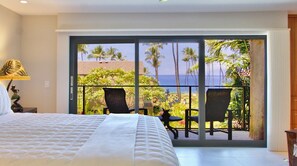 Ein Schlafzimmer mit einem großen Bett, Meerblick und einem Balkon mit Stühlen.