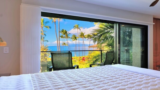 Een slaapkamer met een groot bed, uitzicht op palmbomen en de oceaan, en een balkon met een stoel.
