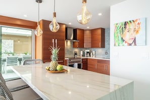 A modern kitchen with a marble island, wooden cabinets, and pendant lighting. - Oceanfront- Supreme Setting (Lahaina)