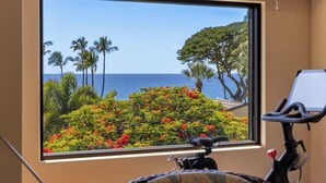 Une pièce dotée d’une grande fenêtre donnant sur un paysage tropical, avec des palmiers et une vue sur l’océan.