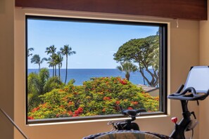 Ein Zimmer mit großem Fenster und Blick auf eine tropische Landschaft mit Palmen und Meer.
