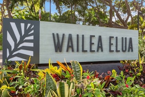Ein Schild mit dem Schriftzug 'WAILEA ELUA', umgeben von verschiedenen Pflanzen.