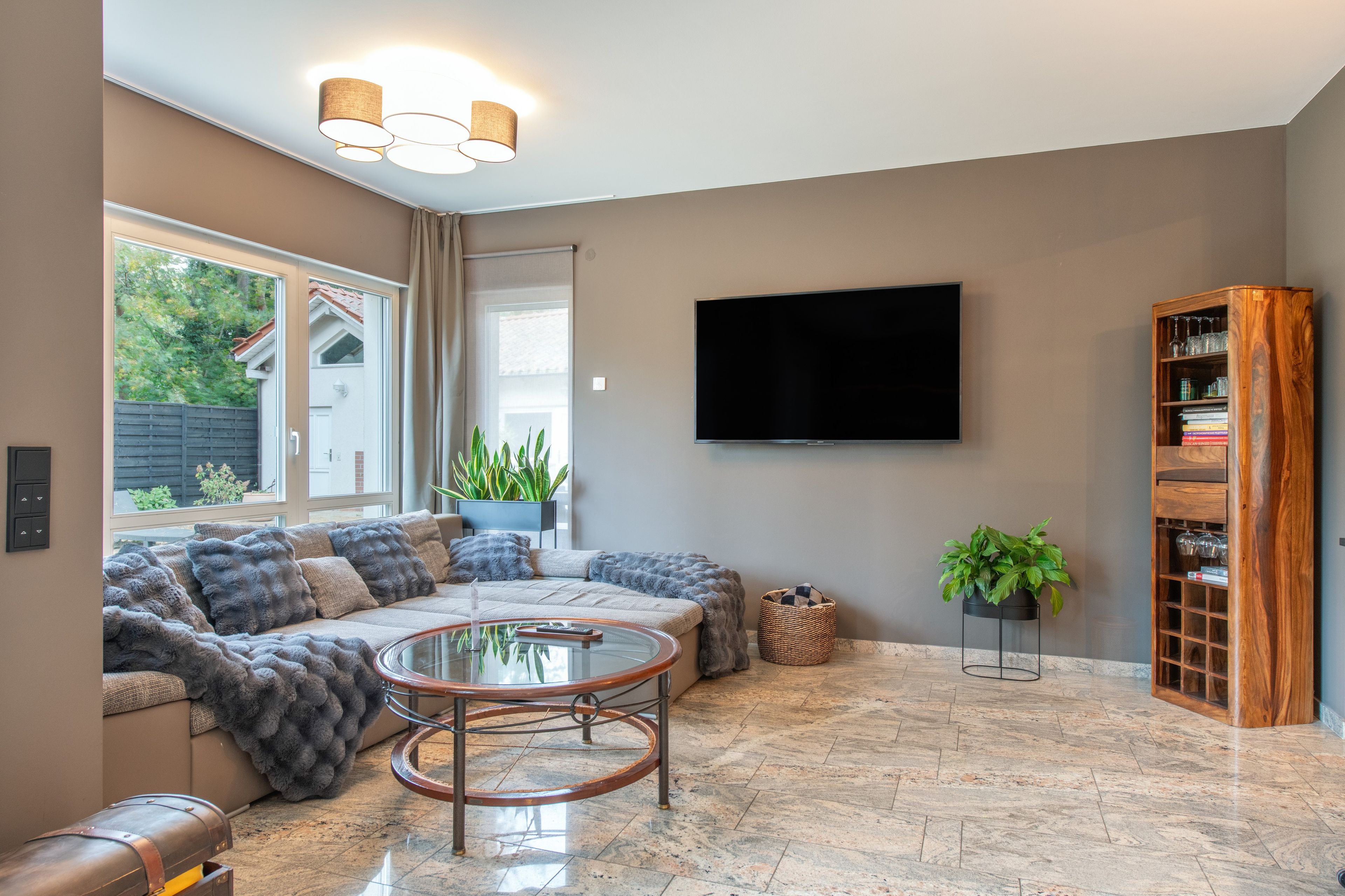 Ein modernes Wohnzimmer mit einer Eckcouch, einem Glastisch, einem flachbildfernseher an der Wand und einem Holzregal.