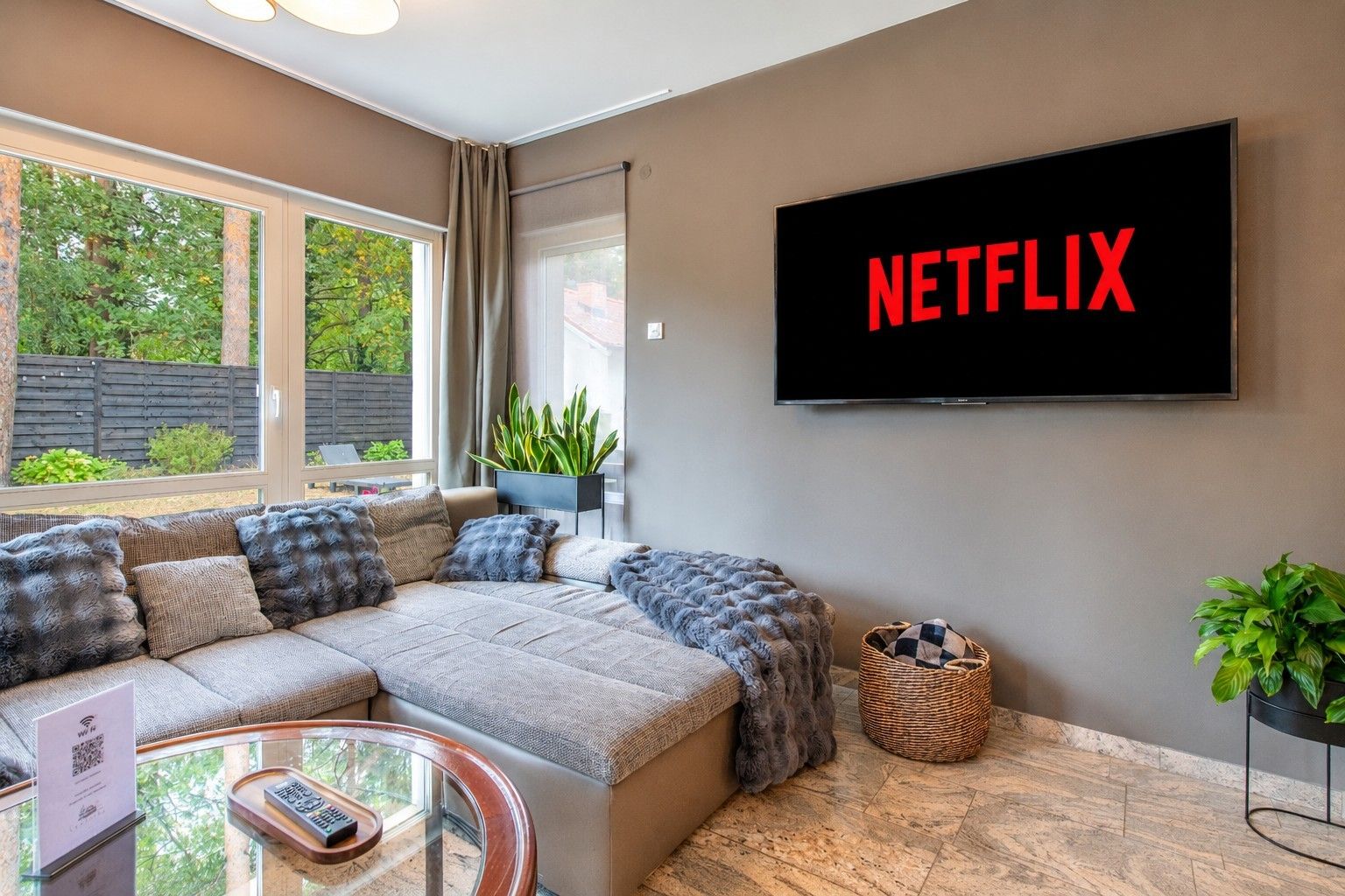 Ein modernes Wohnzimmer mit einer Eckcouch, einem flachbildfernseher an der Wand und einem Glastisch.