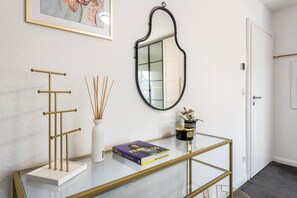 A hallway with a glass table, a gold stand, a framed picture, a mirror, and a door. - Luxury Lakeside Retreat Villa for 11 – Festive Forest Getaway Fireplace & Workspaces, 20 Mins to BER (Bestensee)