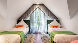 Un dormitorio con dos camas, techo inclinado, cortinas translúcidas y vistas al verdor exterior.