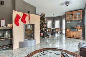 A modern living room with a fireplace, a Christmas tree, and a dining area with a wooden cabinet and glassware. - Luxury Lakeside Retreat Villa for 11 – Festive Forest Getaway Fireplace & Workspaces, 20 Mins to BER (Bestensee)
