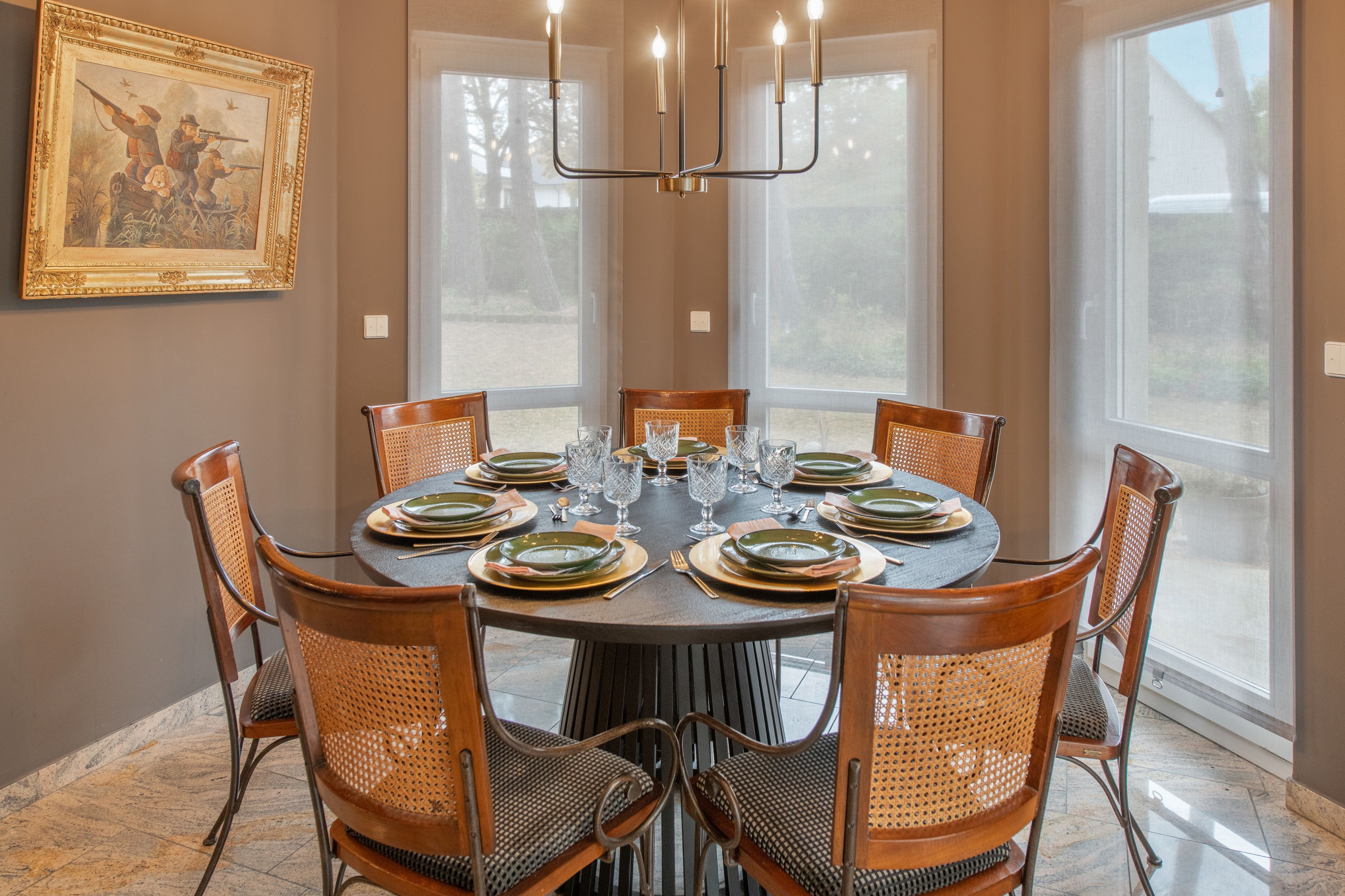 A dining room with a round table set for six, surrounded by wicker chairs.