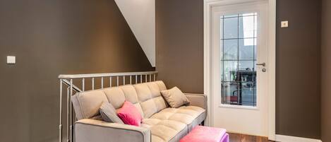 A modern living room with a grey sofa, a pink ottoman, and a staircase leading to a second floor.