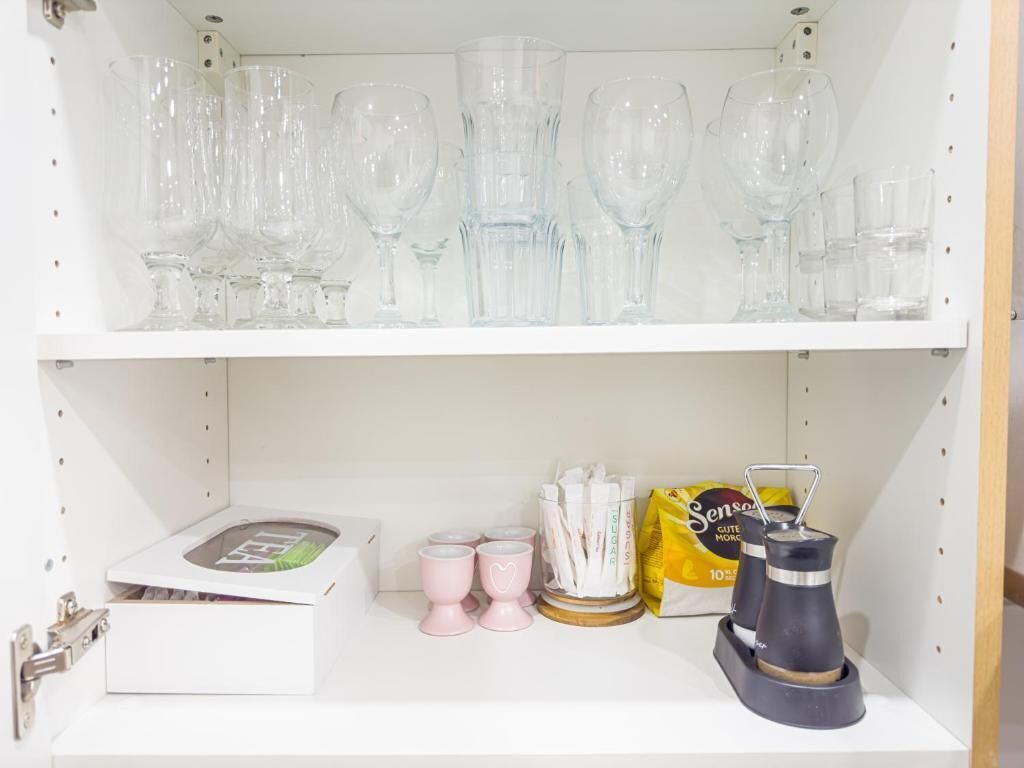 Une étagère avec des verres transparents, une boîte blanche, des tasses roses, une machine à café et un paquet de café.