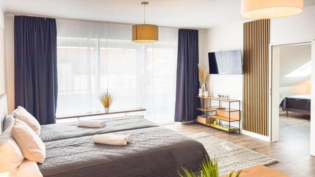 A modern hotel room with a large bed, a desk, a chair, a TV, and a large window with curtains. - Luchtbergstraße 1 (Bremen)